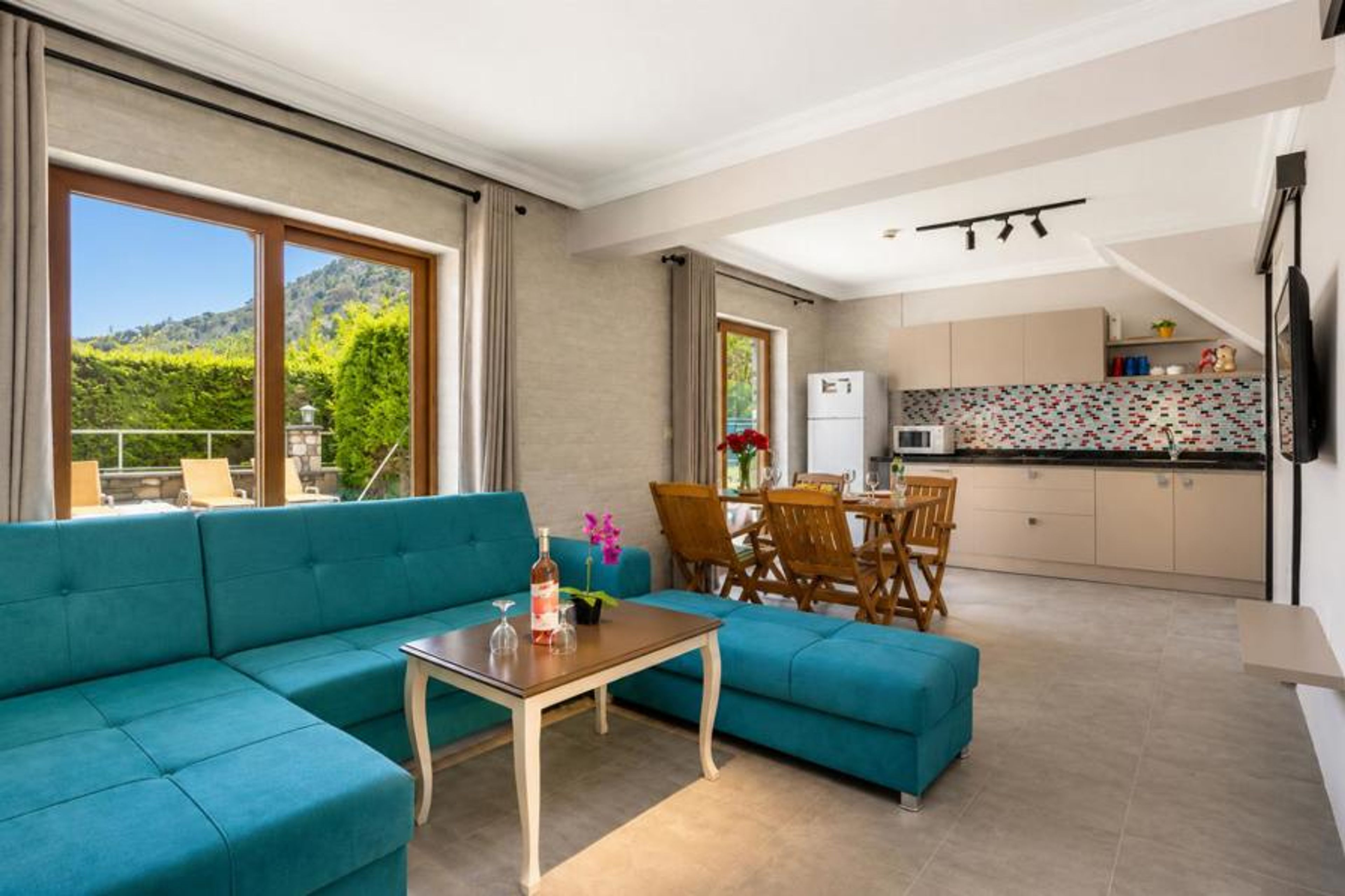 A modern, open-concept living space and kitchen featuring a vibrant turquoise sectional sofa as the central focus.