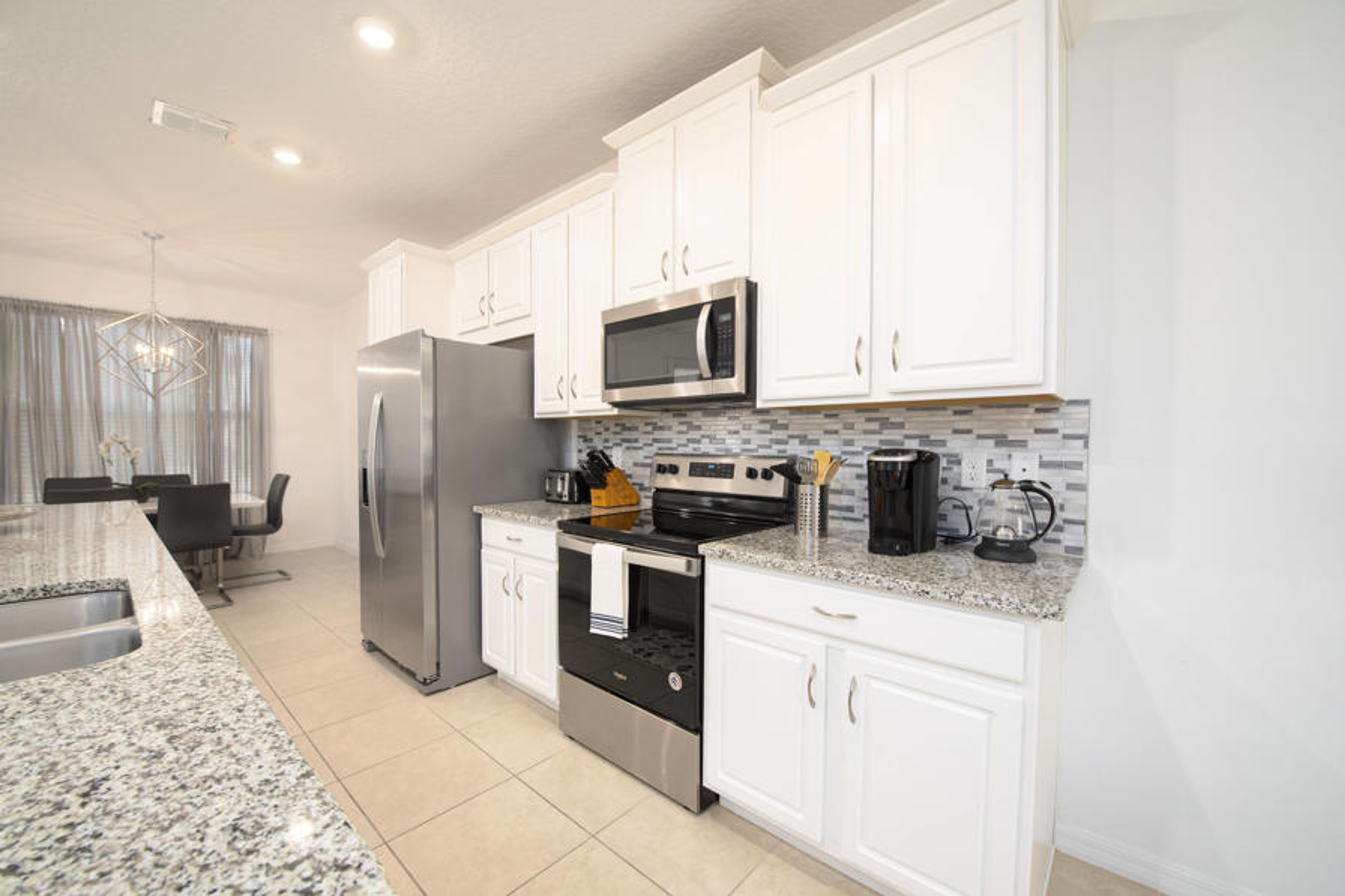 Discover culinary creativity in this sleek kitchen, featuring polished granite counters and crisp white cabinetry. Modern stainless-steel appliances and a stylish tiled backsplash enhance your cooking adventures.