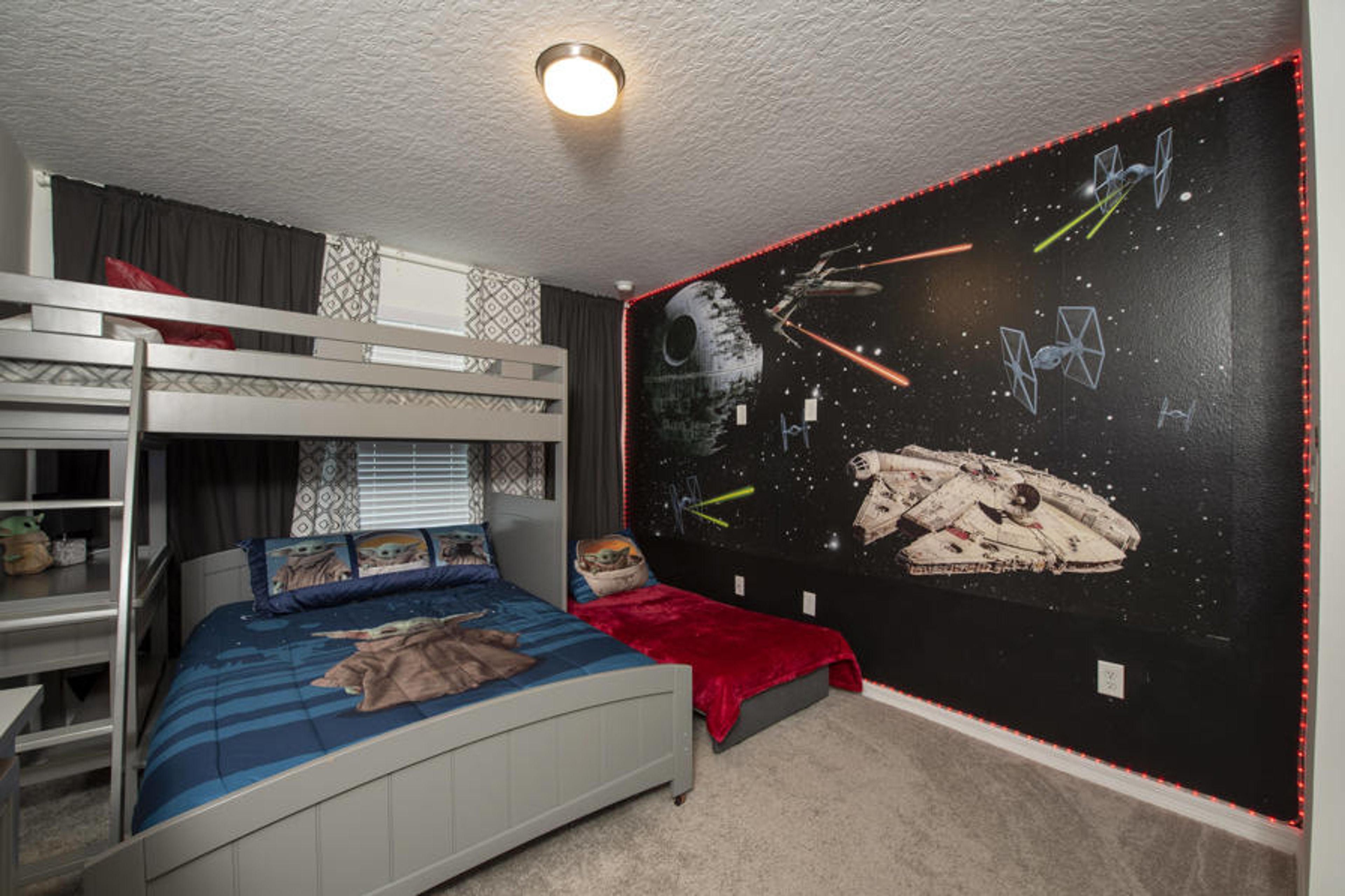 This fun bedroom features a stylish bunk bed for kids, a cozy blue quilt, and vibrant red accents. A space-themed mural adds adventure, while the soft carpet invites relaxation after a day filled with excitement.