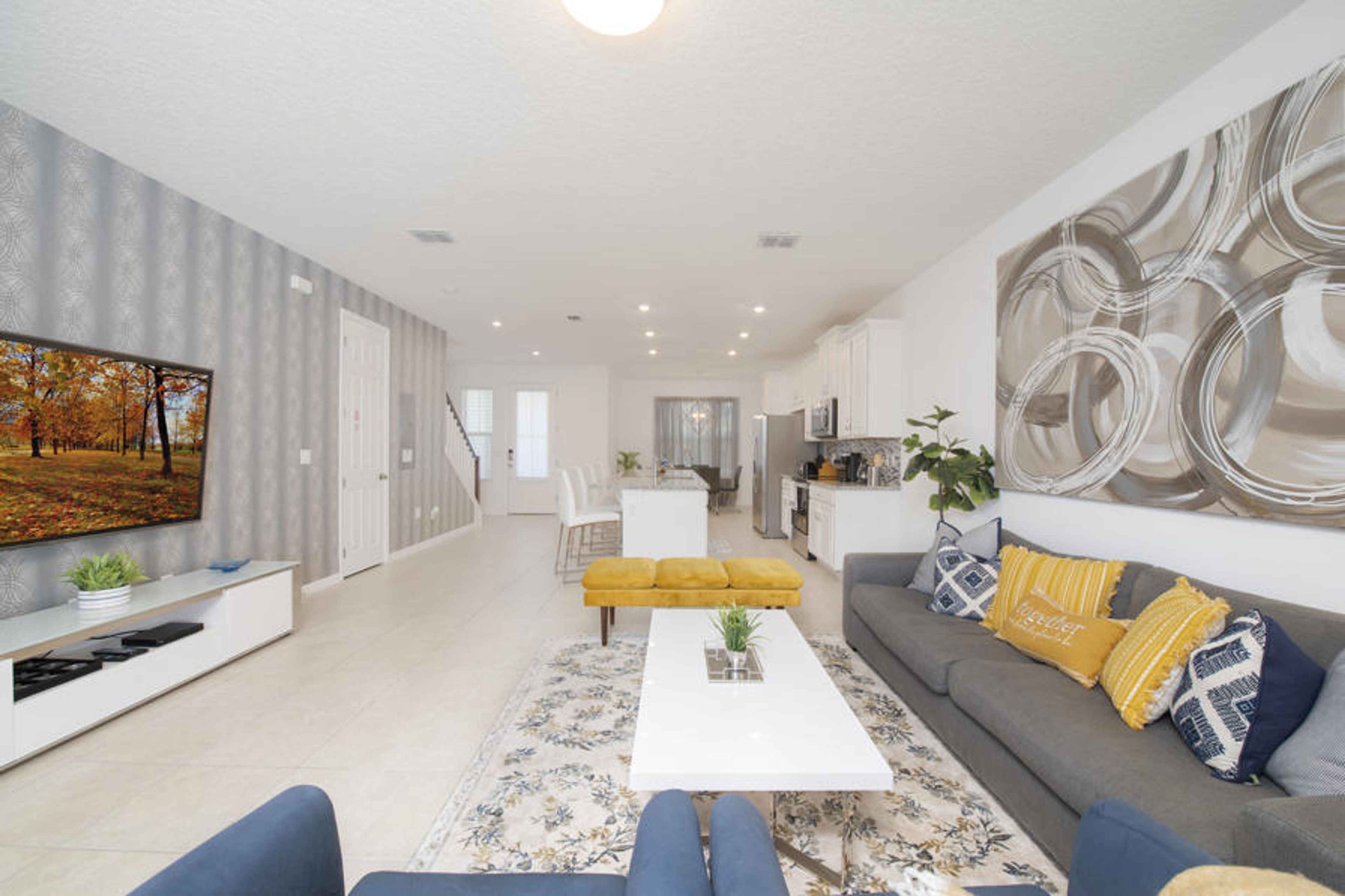 Relax in our stylish living room with a sleek gray sofa and vibrant yellow cushions. The open layout leads to a bright dining area featuring modern fixtures and a chic coffee table, creating a warm and welcoming atmosphere.