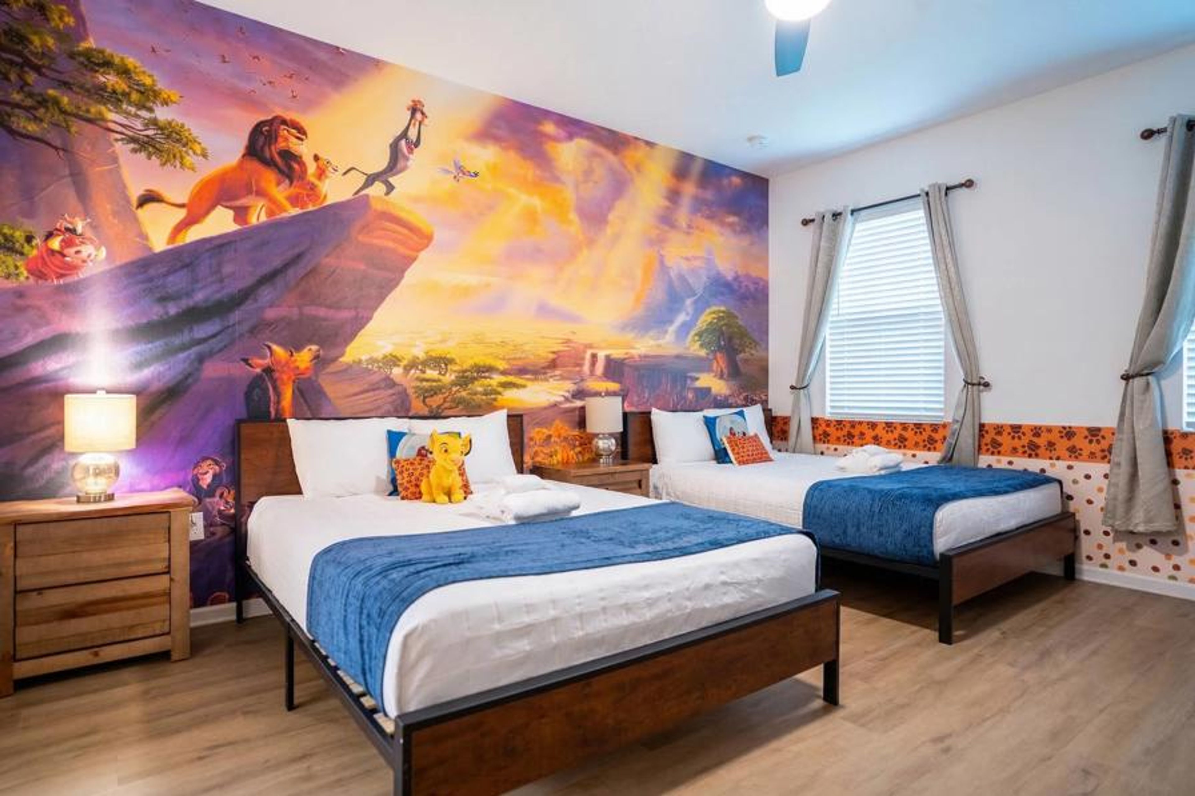 Rest in a bright safari-themed bedroom with two cozy beds, blue accents, wood furniture, and a colorful savanna mural. Natural light, soft bedding, and playful details create a fun and comfortable space for kids or family guests.