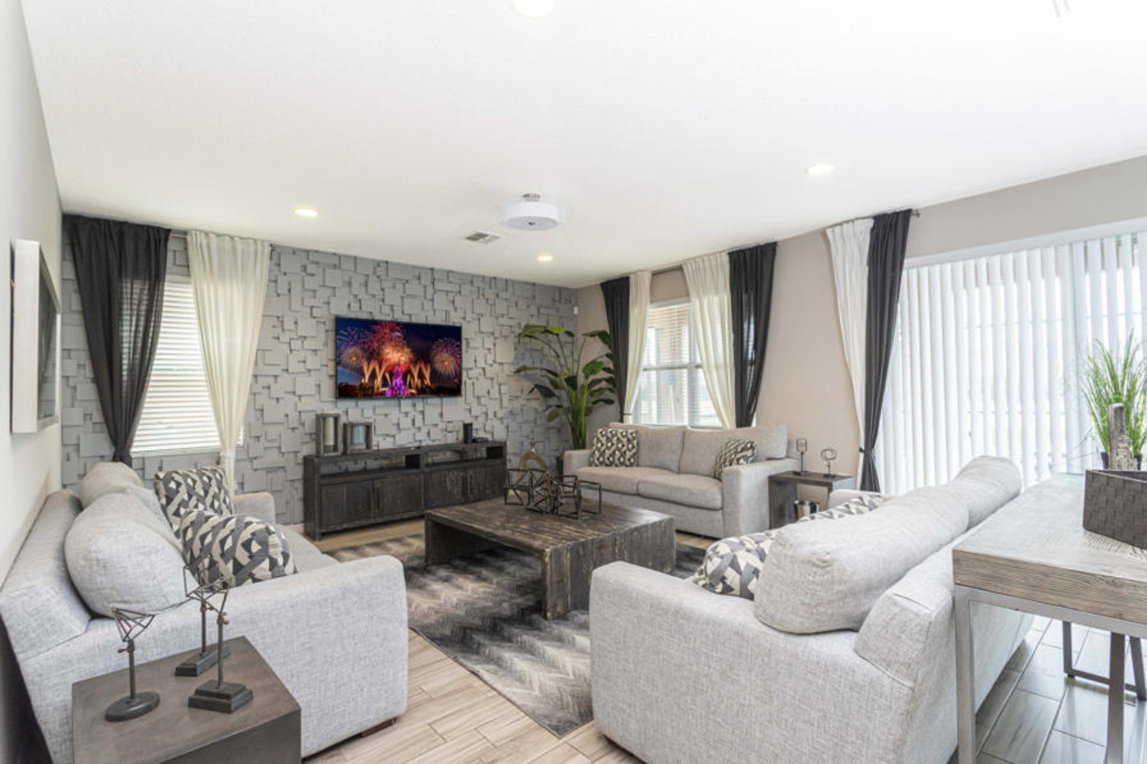 Welcome to a bright living area with soft gray sofas and a stylish accent wall. Large windows dressed in elegant curtains let in natural light, creating an airy space for you to unwind after a day of adventure.