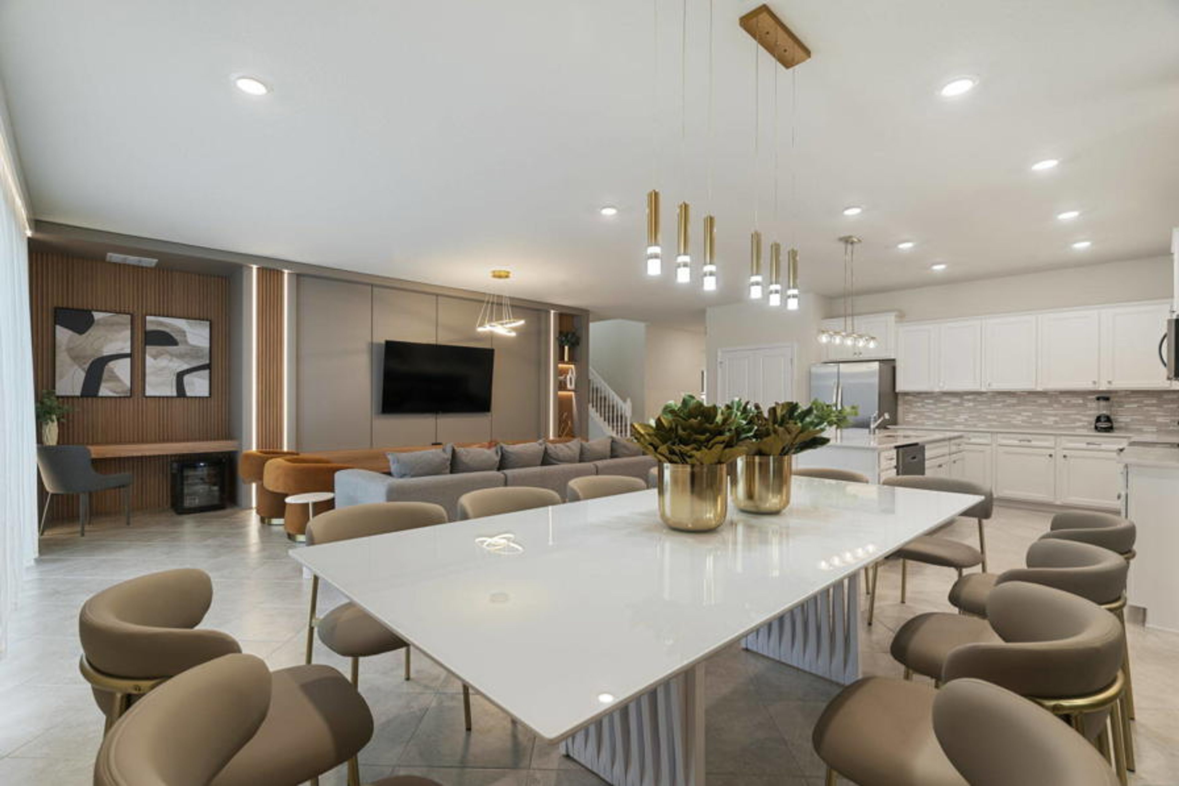 Experience our inviting dining area with a sleek white table and cozy rounded chairs perfect for gatherings. Elegant pendant lights add warmth to the modern decor, seamlessly connecting to the kitchen for a delightful atmosphere.