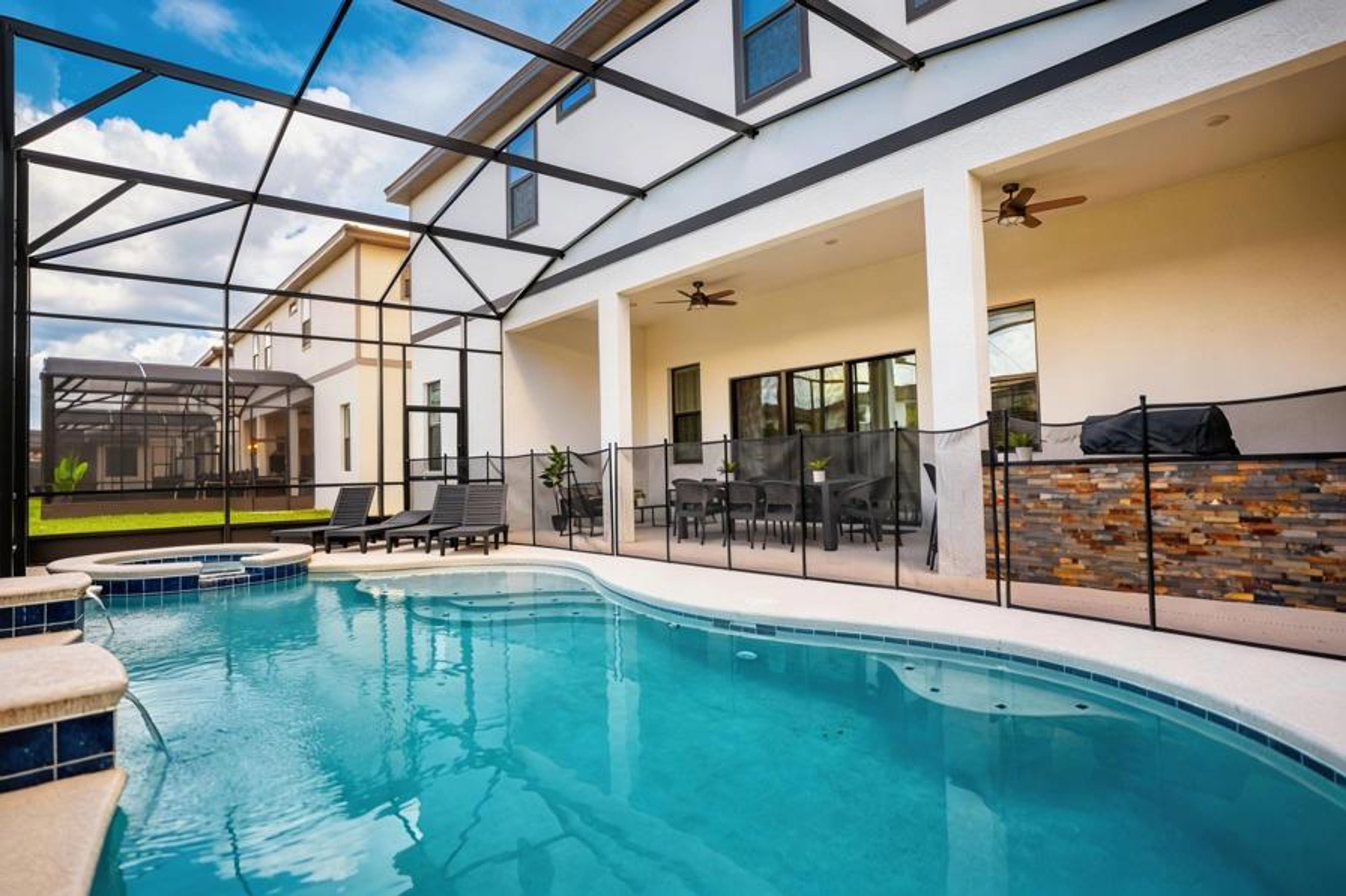 Step outside to your personal oasis, featuring a stunning pool surrounded by sleek tiles and a stylish enclosure. Relax on lounge chairs or enjoy cozy evening chats in the inviting seating area, all under the bright blue sky.