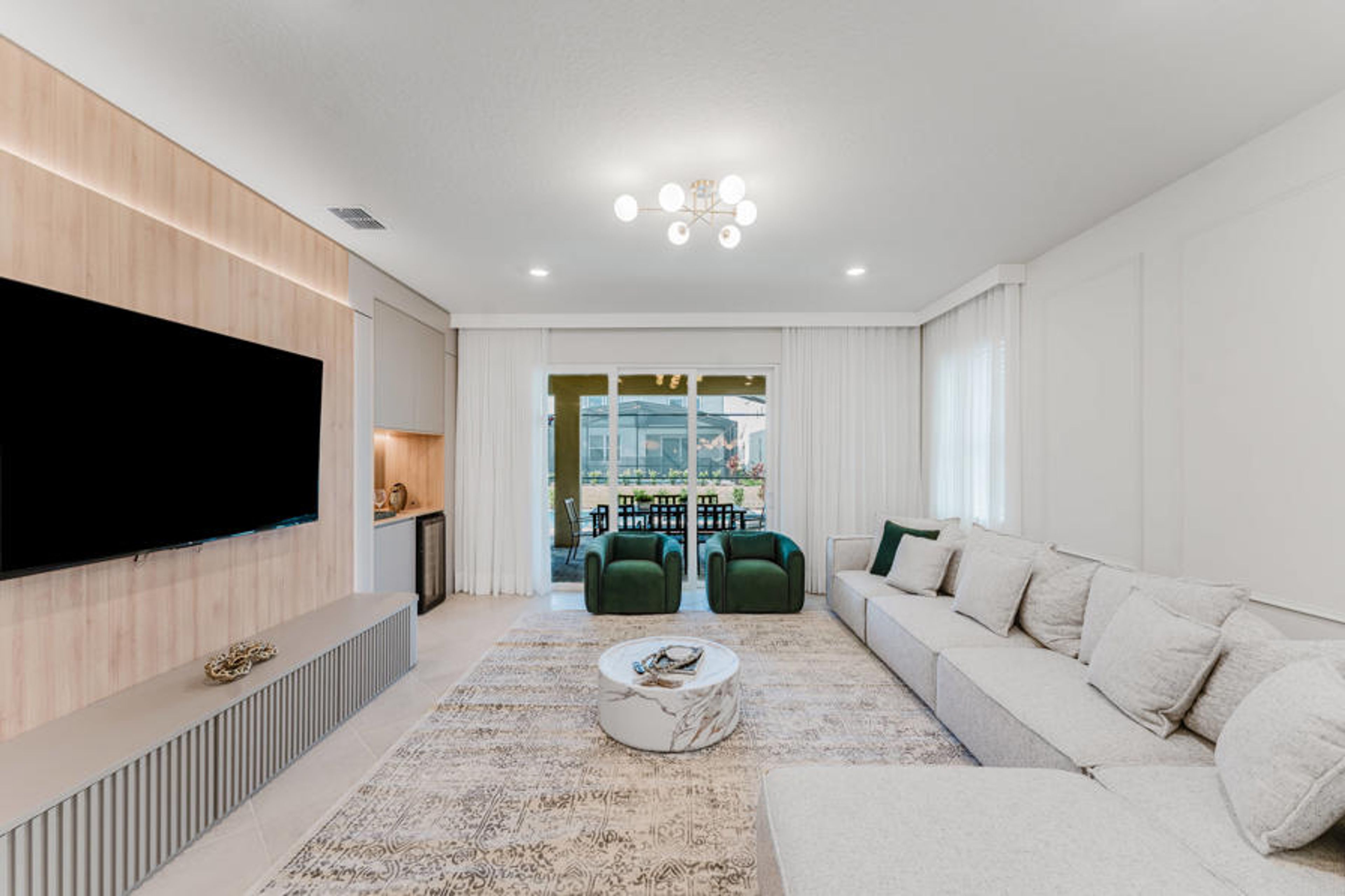 Enjoy a stylish living room with a plush white sectional and chic round coffee table, perfect for gatherings. Sunlight floods in through large glass doors, highlighting the soft textures and modern decor for a cozy atmosphere.
