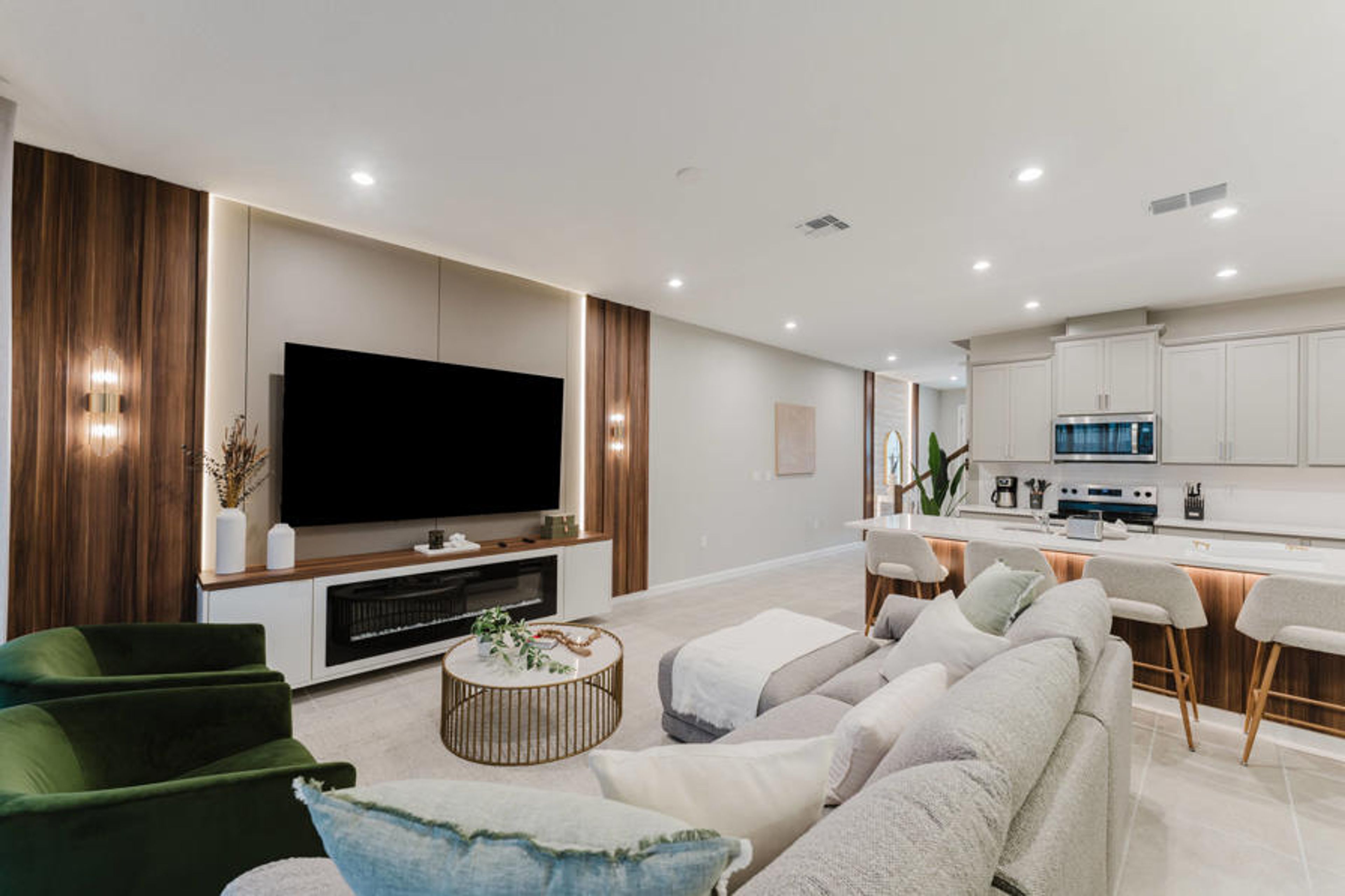 Experience comfort and style in our spacious living area, featuring a cozy sectional sofa and vibrant green armchairs. The sleek entertainment unit and modern kitchen with bar seating make it ideal for gatherings and relaxation.