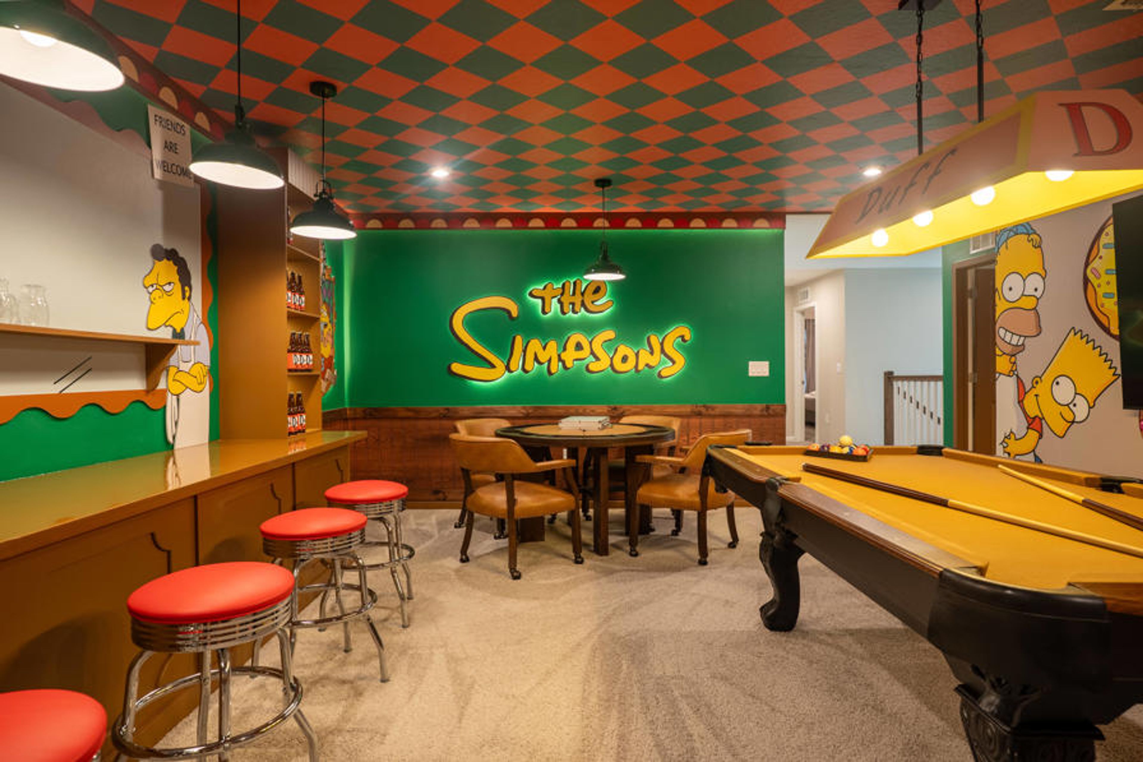 Step into a vibrant game room featuring playful "The Simpsons" murals and a striking checkerboard ceiling. With cozy red barstools and a classic pool table, this space invites lively gatherings and friendly competition.
