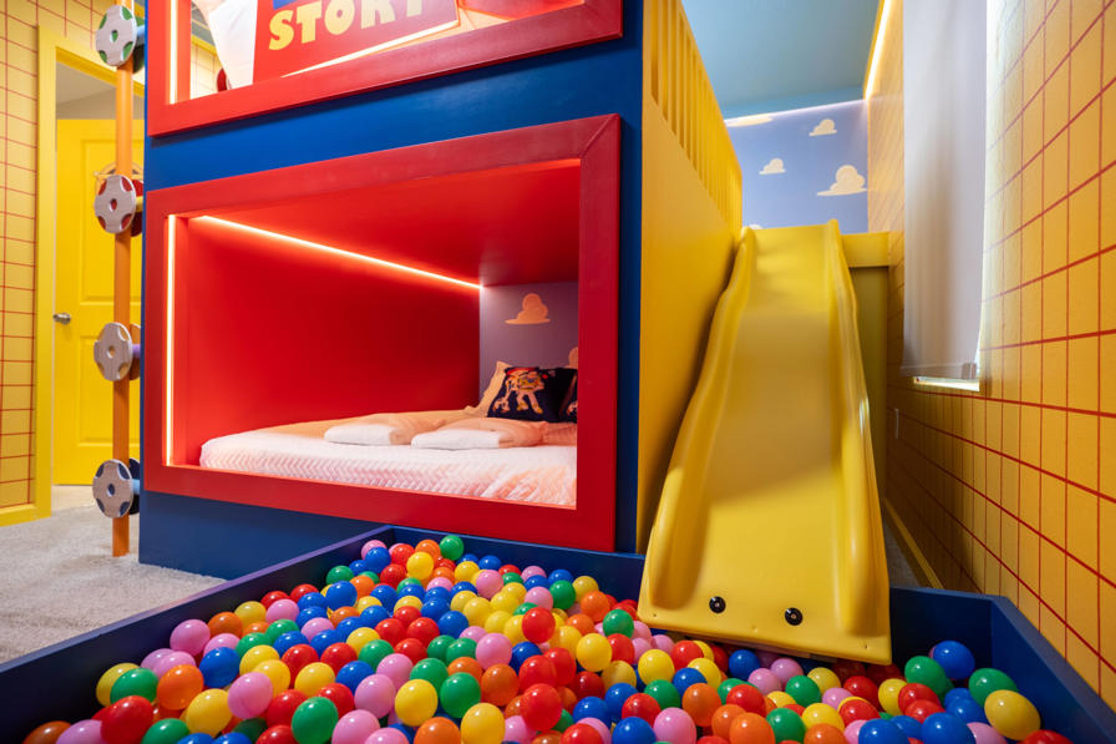 This vibrant children's bedroom features a cozy sleeping nook with red accents and a fun yellow slide. A soft bed is surrounded by a cheerful array of colorful balls, promising endless entertainment and joy for your little ones.