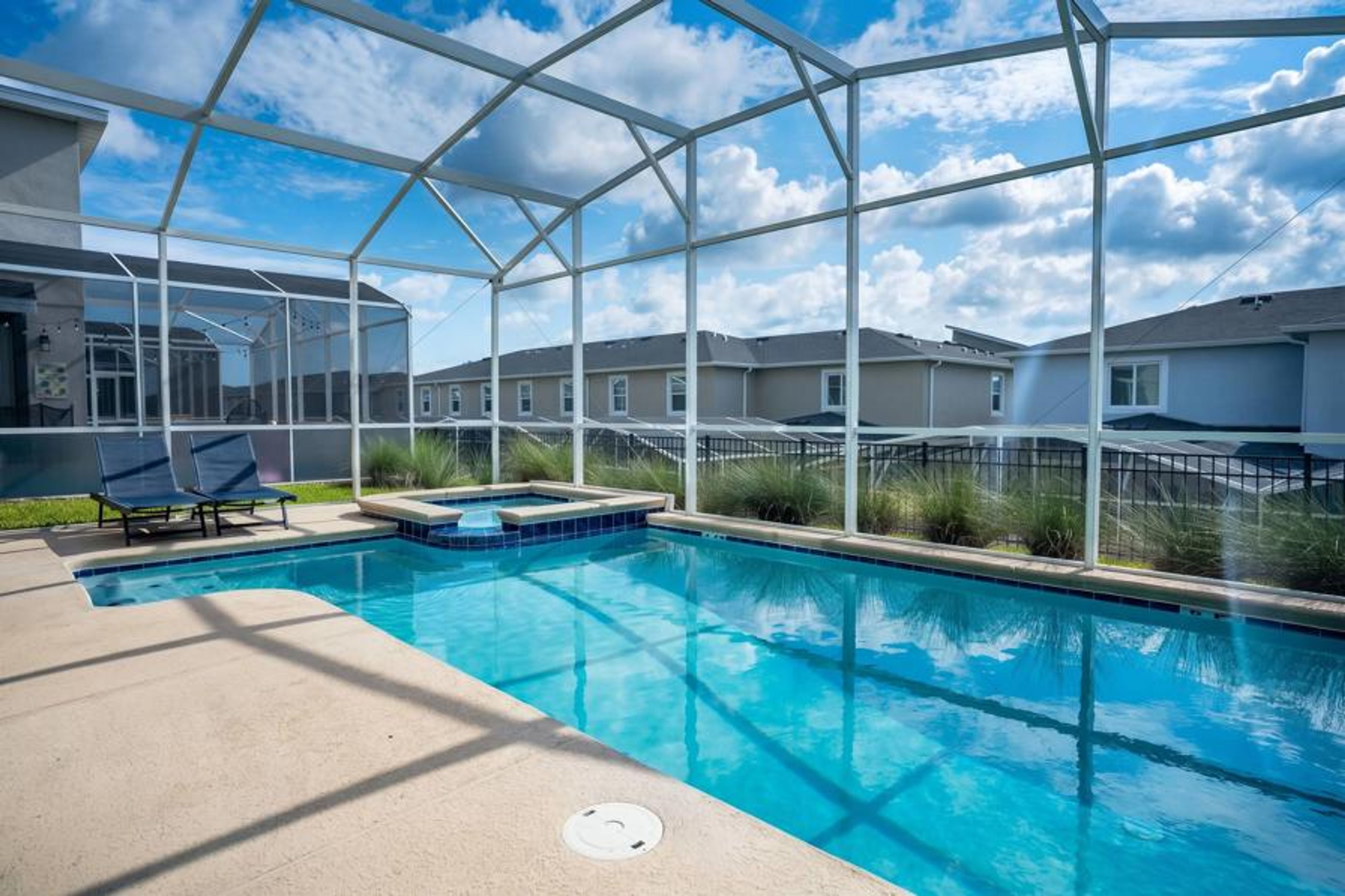 Relax in a private screened pool area with sparkling water, a raised spa, lounge chairs, open sky views, and peaceful surroundings, creating a refreshing space for family vacation moments.