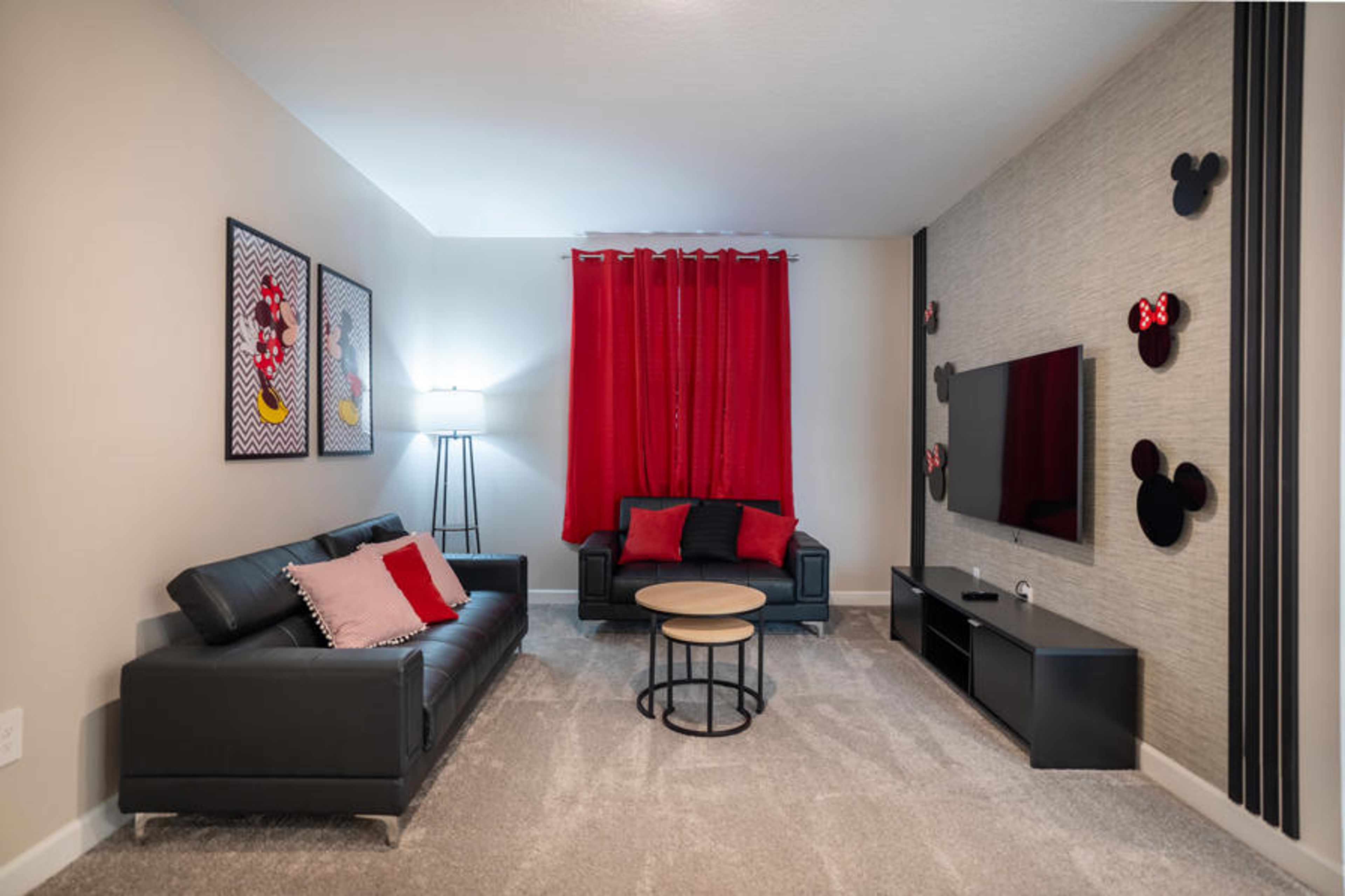 This cozy living area features a sleek black couch with vibrant red pillows, inviting you to relax after your adventures. Bold red curtains and charming decor create a warm, playful atmosphere for unwinding and enjoying your stay.