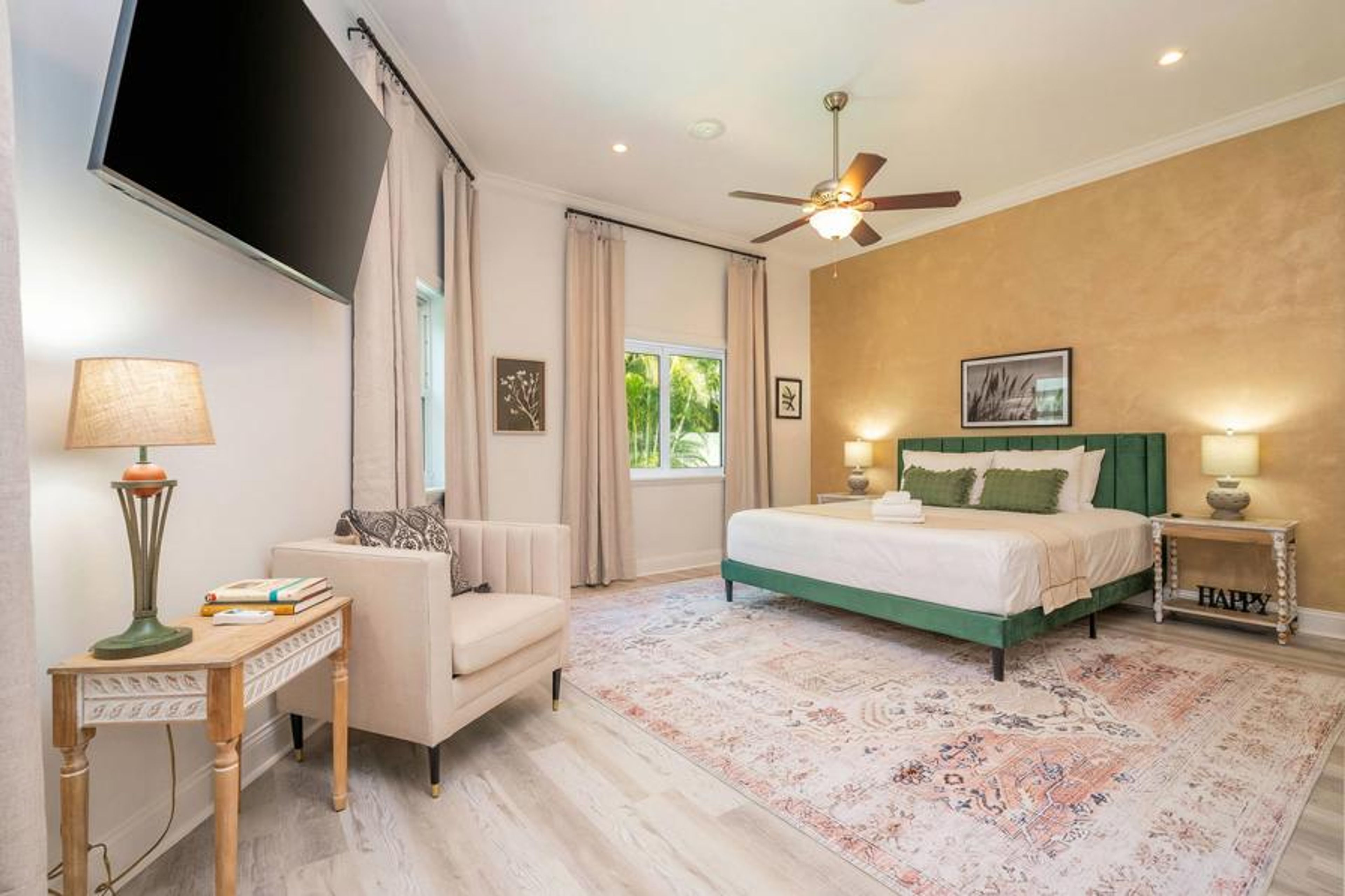 Enjoy the gentle natural light streaming through large windows in this charming bedroom, featuring a plush bed and a calming palette of greens and neutrals that offer a serene atmosphere ideal for relaxation.