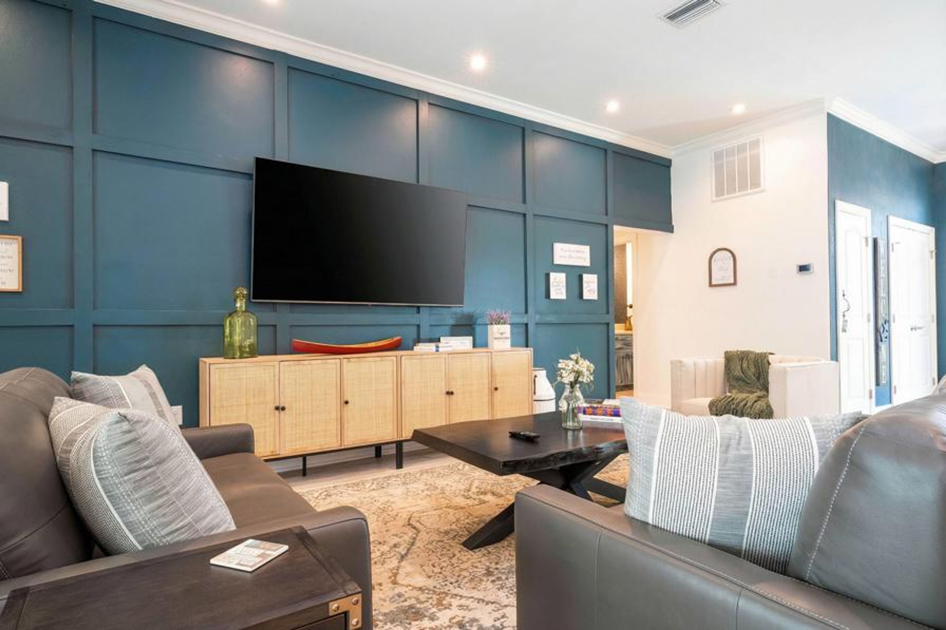 Enjoy a stylish living area with a striking navy accent wall, a plush grey sofa, and a chic coffee table. Warm wood cabinetry and soft lighting create a cozy atmosphere, ideal for your relaxation and comfort.