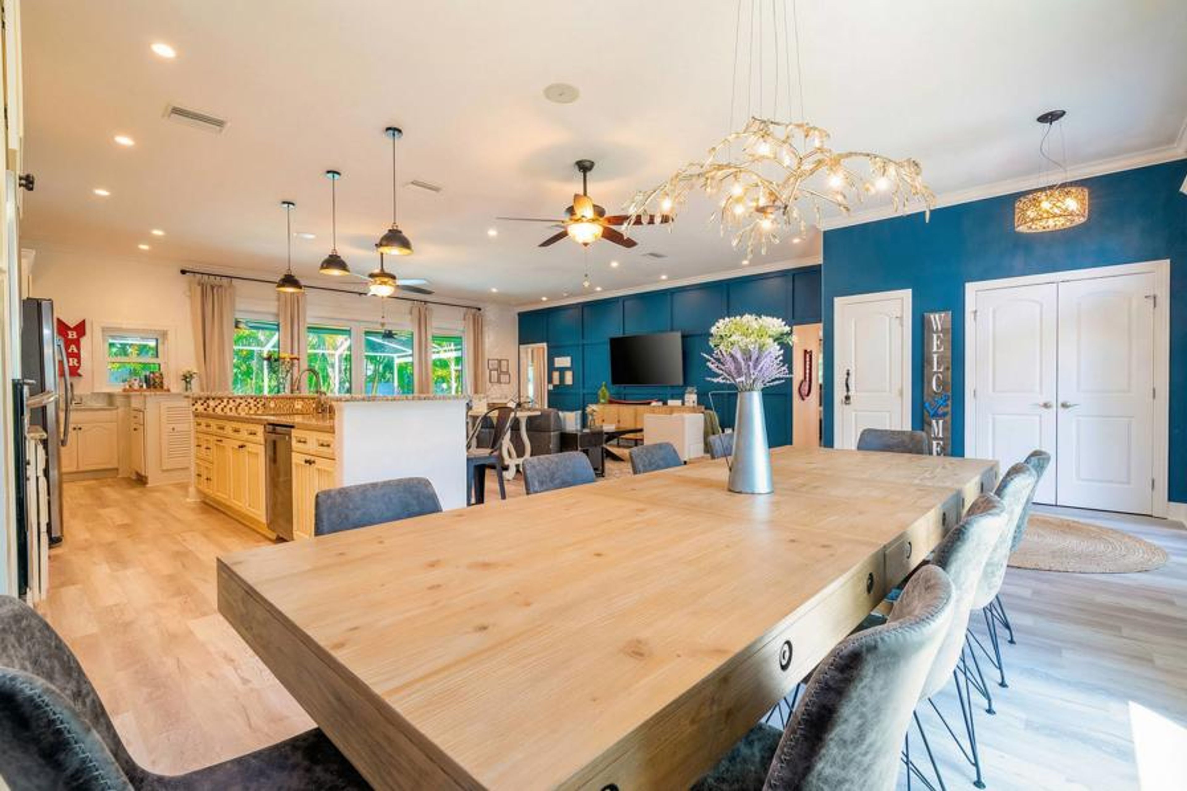Dine in style at the expansive wooden table, surrounded by plush gray chairs, while natural light floods the open layout. The striking blue accent wall and modern lighting create a vibrant yet cozy atmosphere for gatherings.