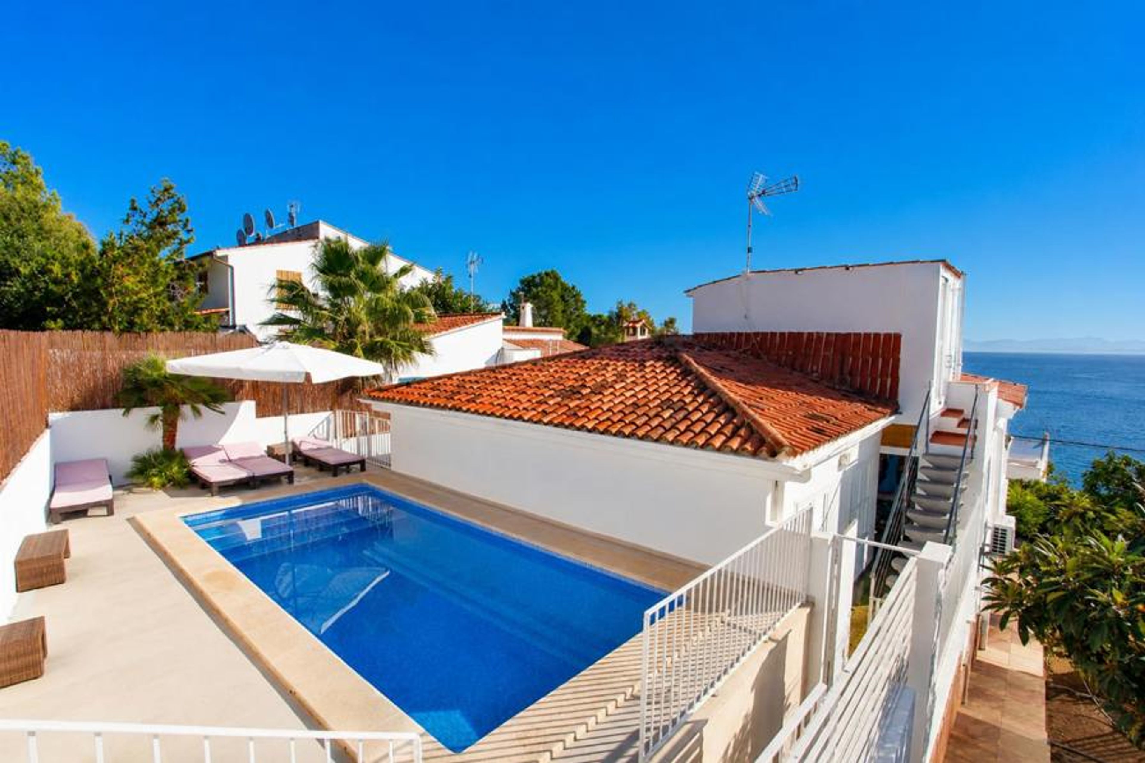 A private swimming pool and sun terrace sit alongside a terracotta-tiled roof, offering coastal views of the sea under a clear blue sky.