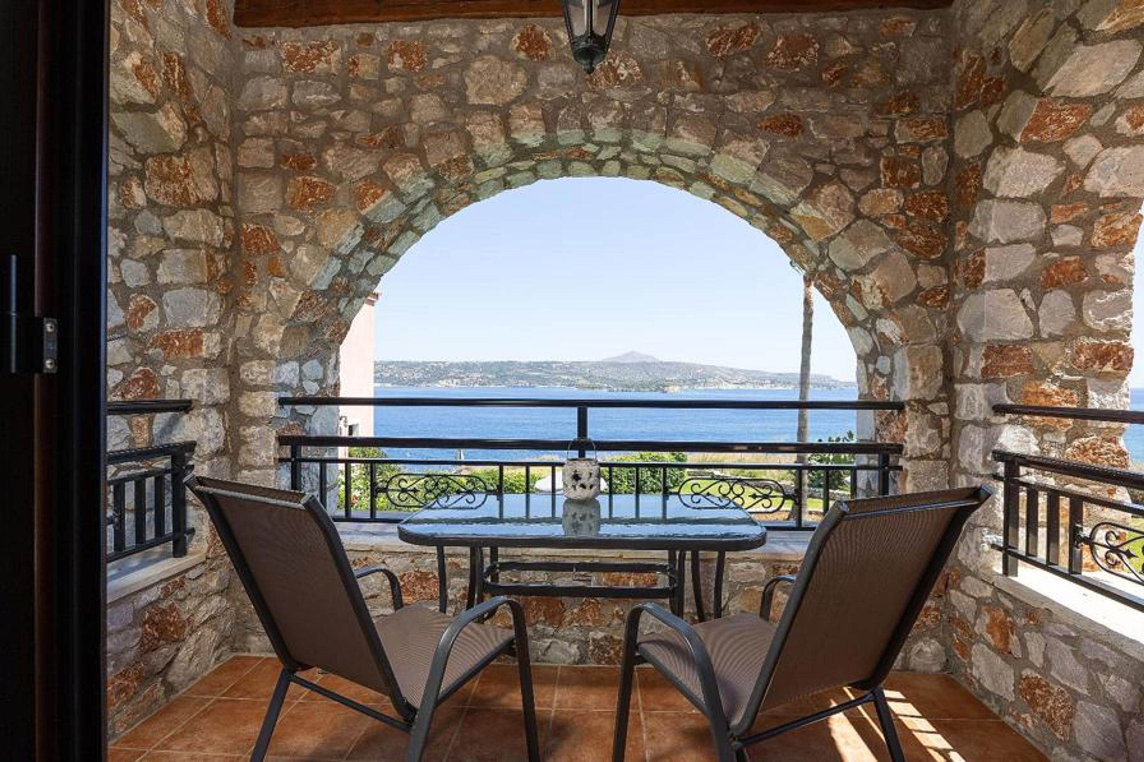 An interior-to-outdoor view from one of the villa’s upper-level stone balconies, framing a picturesque coastal scene.