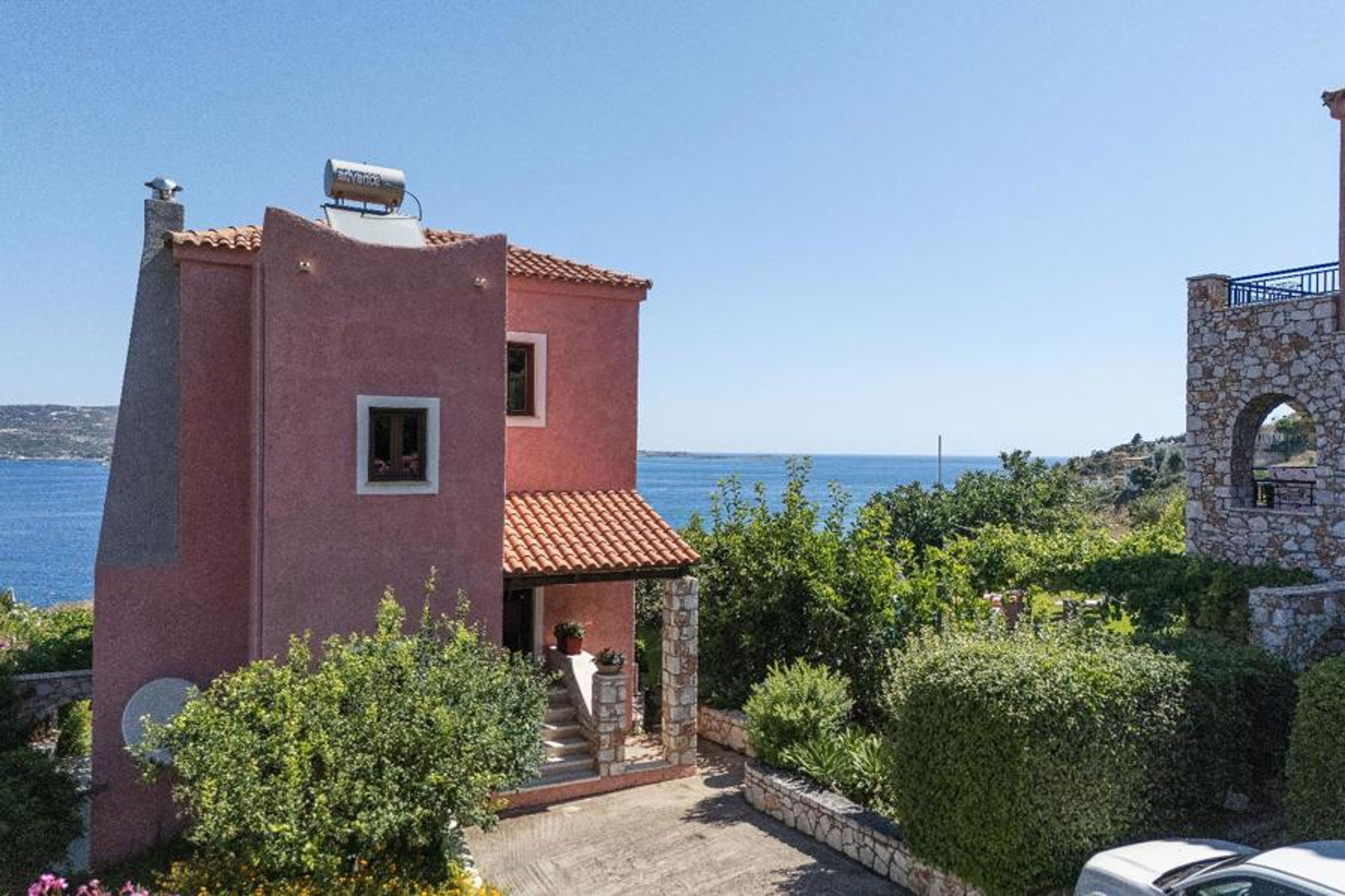 A elevated exterior view of the multi-level villa property, showcasing the front entrance and its proximity to the coastline.