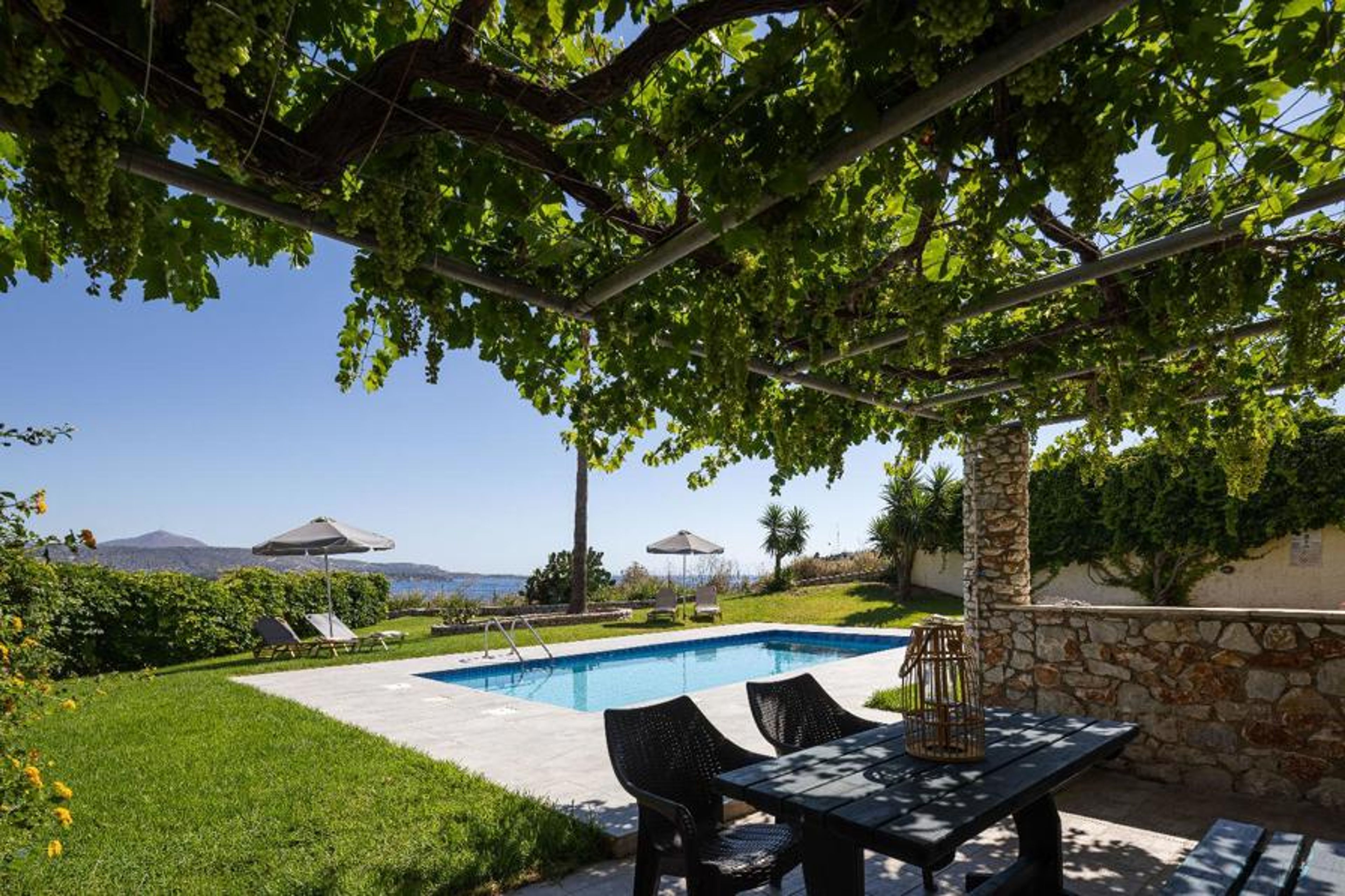 An alternate view of the villa's outdoor area, captured from underneath a shaded pergola to highlight the outdoor dining space and scenic backdrop.