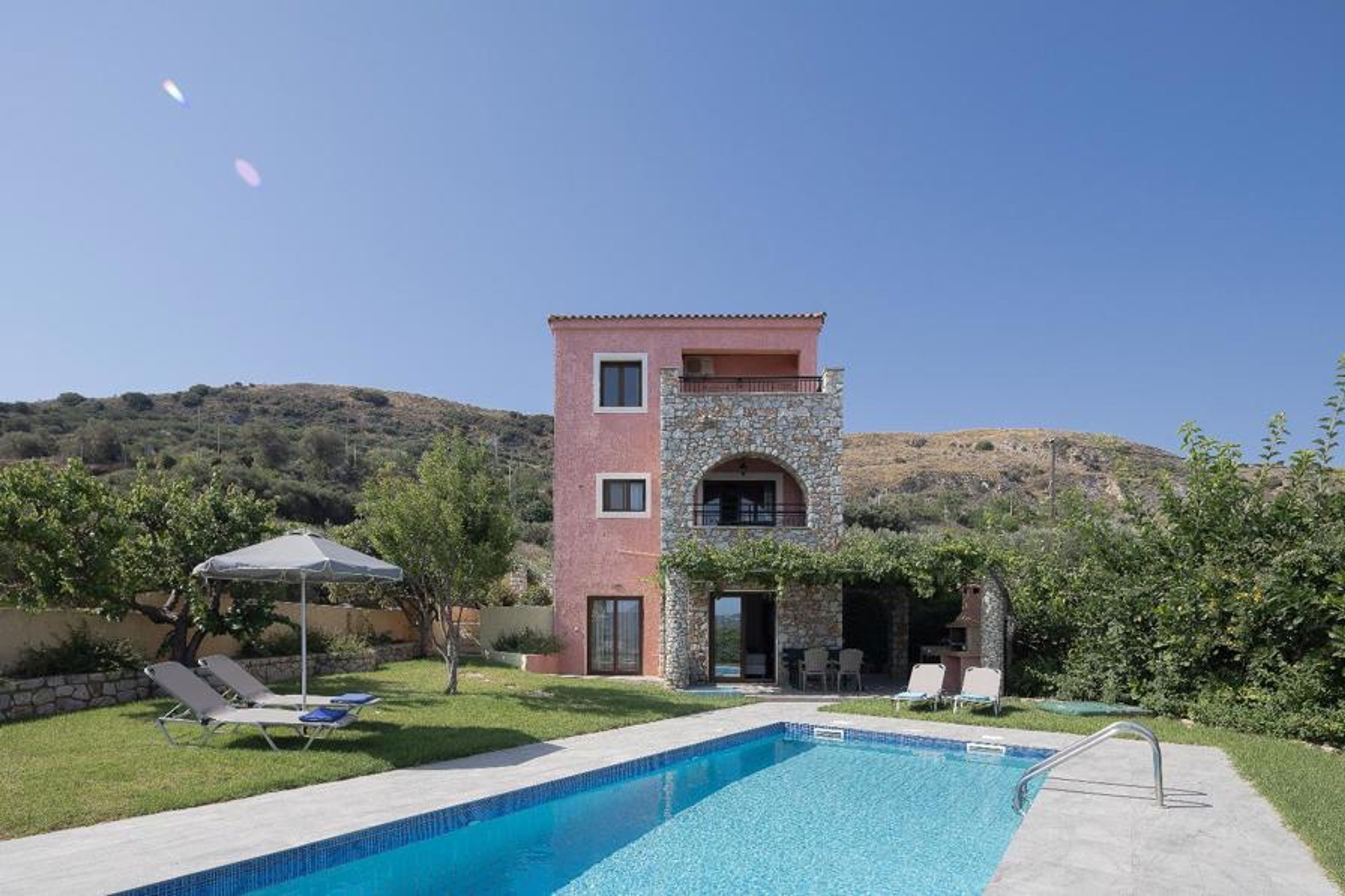 Charming Mediterranean villa with a private swimming pool, spacious lawn, sun loungers, shaded outdoor seating, and peaceful hillside surroundings.