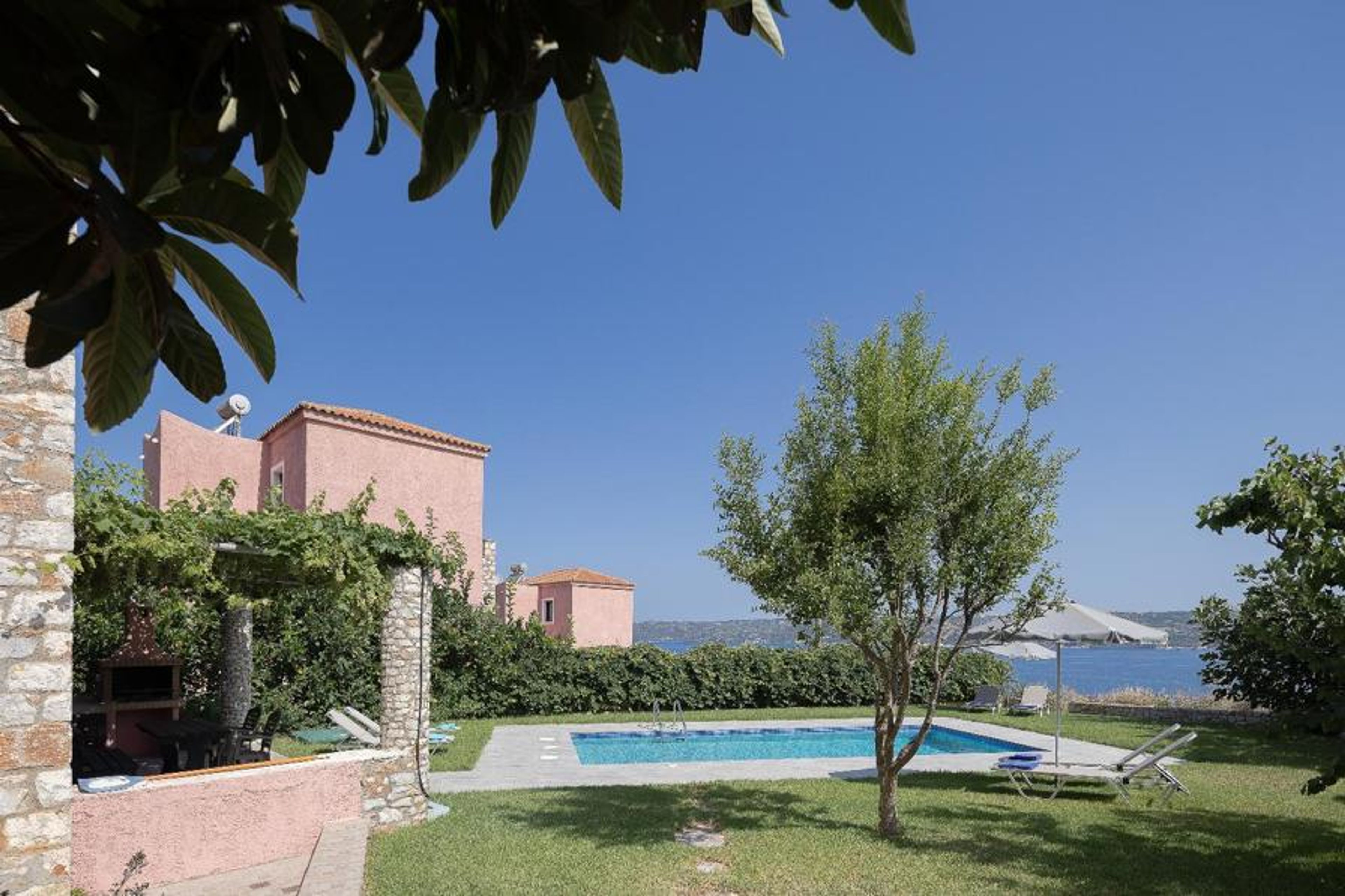 Mediterranean villa garden with a private swimming pool, sun loungers, shaded barbecue area, and beautiful sea views.