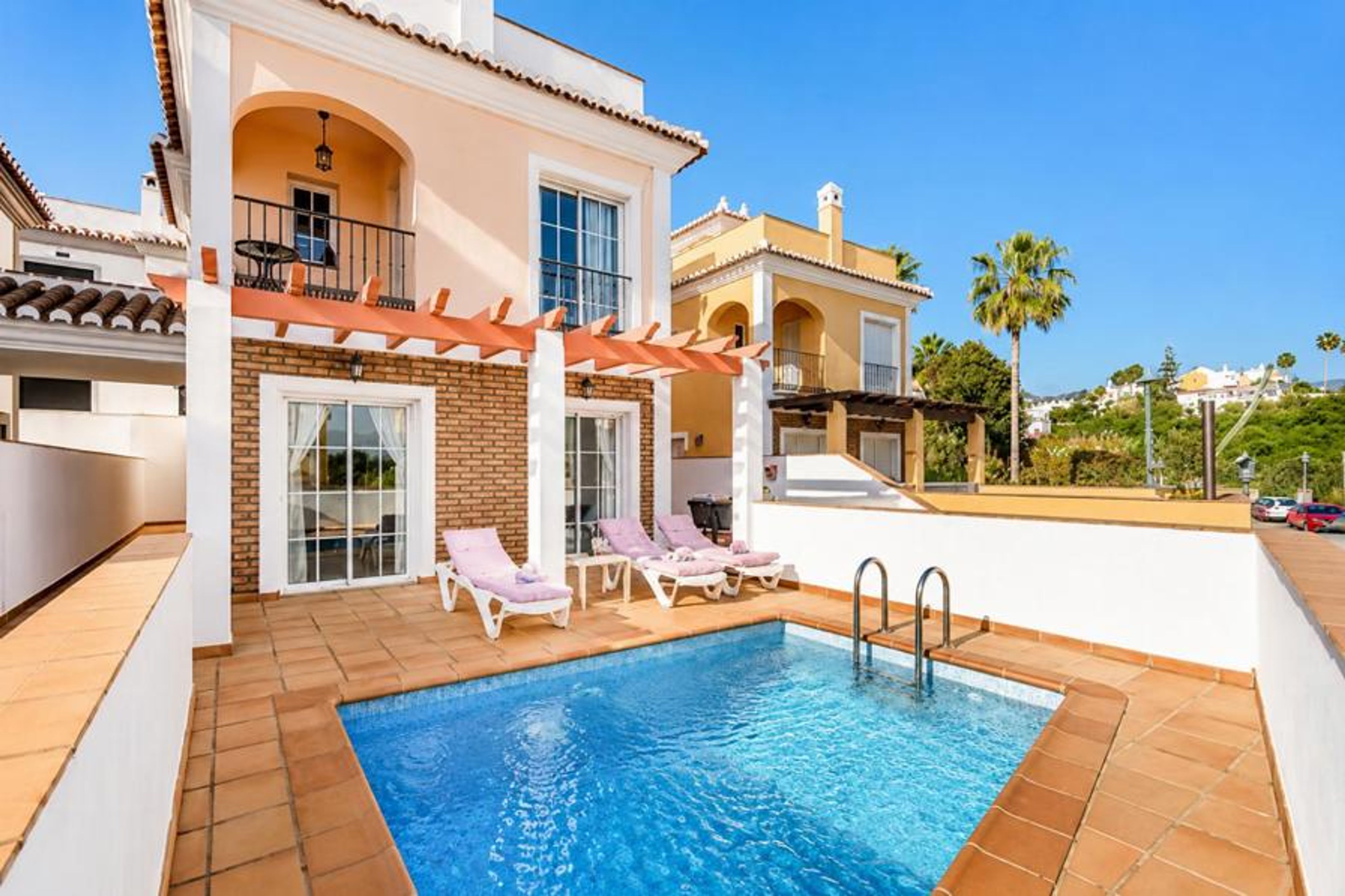 Luxury multi-story townhouses with a private turquoise swimming pool, sun loungers, and tiled terraces against a clear blue sky.