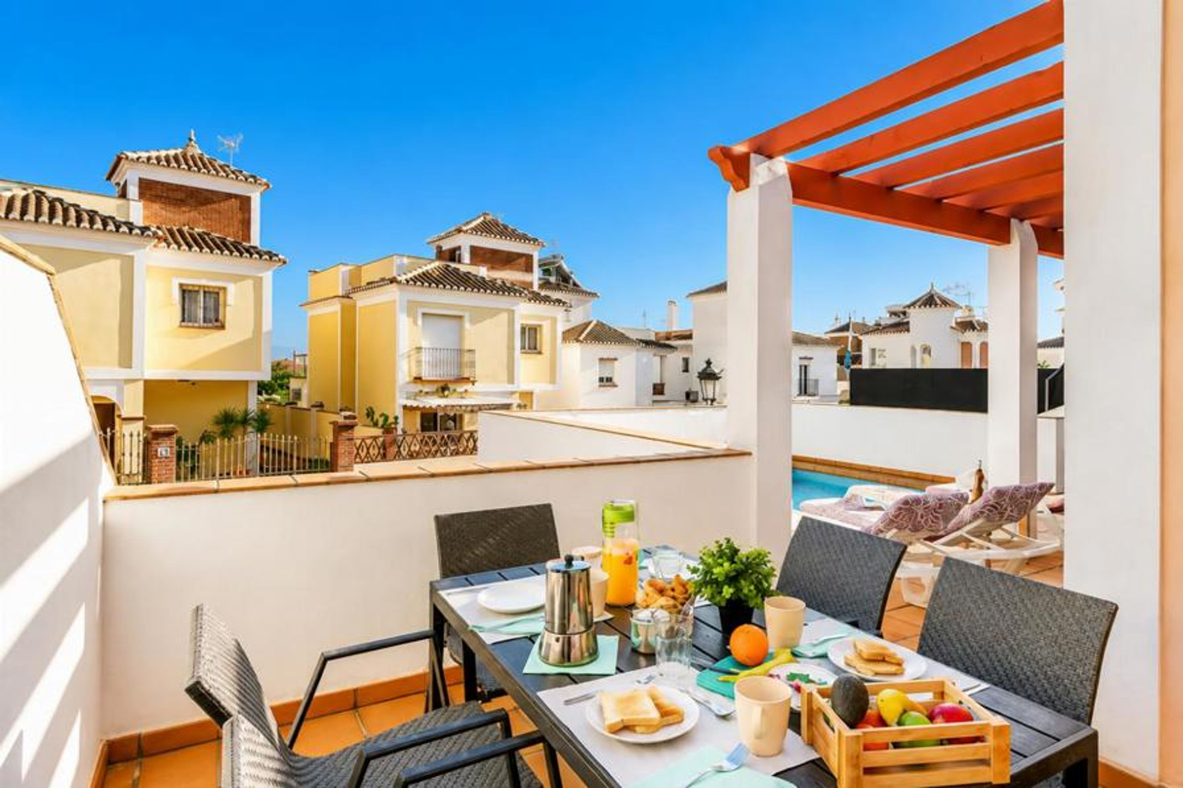 Scenic alfresco dining area on a luxury villa terrace, featuring a modern black dining table beautifully set for breakfast next to a private pool deck with stunning Mediterranean-style townhouse views.
