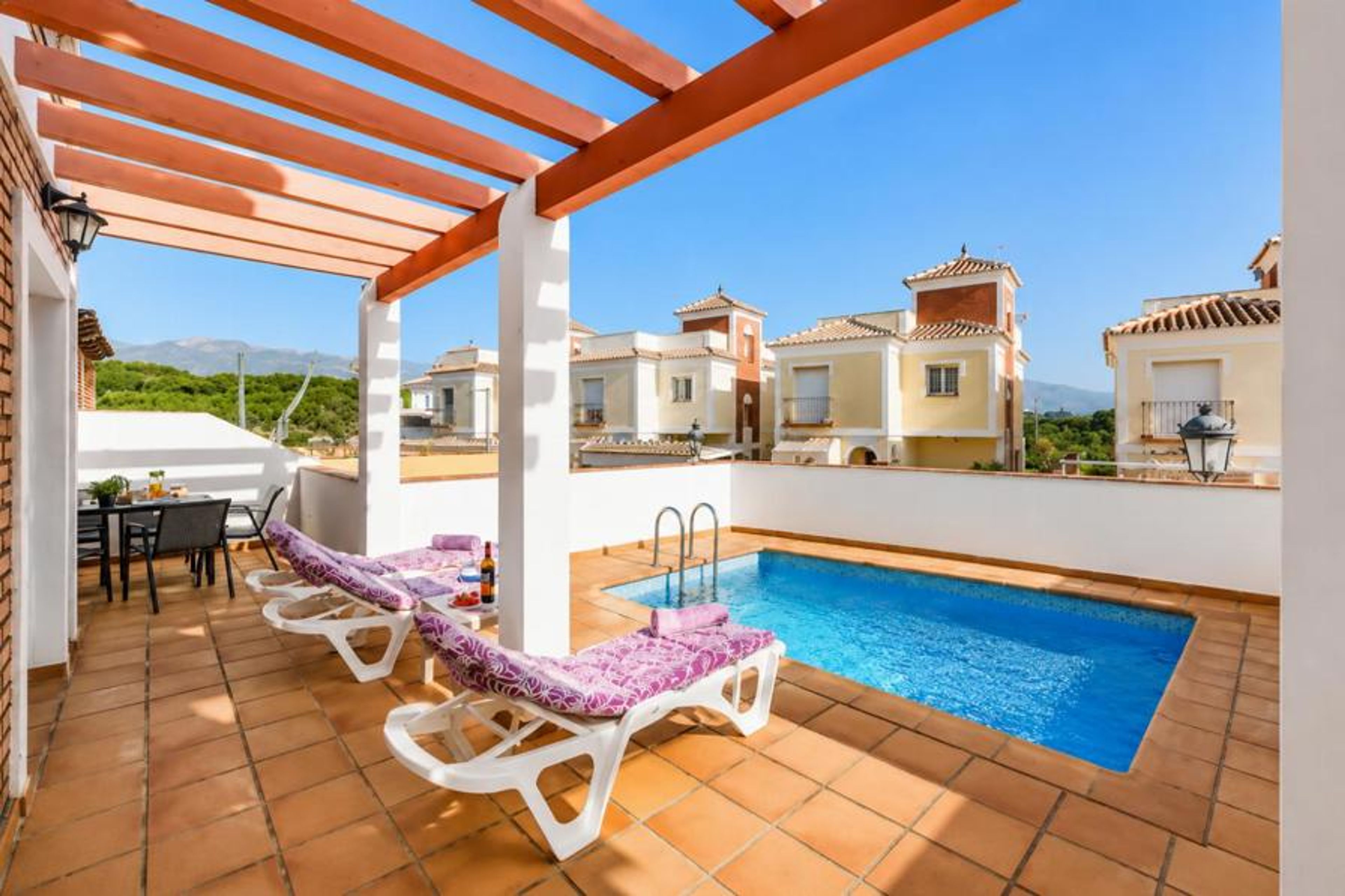 Spacious rooftop terrace at a modern villa townhome, featuring a private swimming pool, plush sun loungers under a wooden pergola canopy, an alfresco dining table, and panoramic residential views.